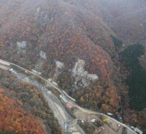 温湯地区の山腹崩壊状況写真（中腹付近が数カ所大きく崩壊して下の道路に岩塊落下している）